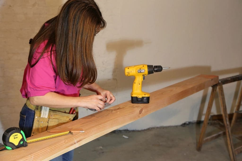 Persona midiendo y perforando un tablón de madera en un taller